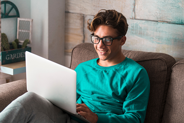 Male high school student sitting on a couch using a laptop