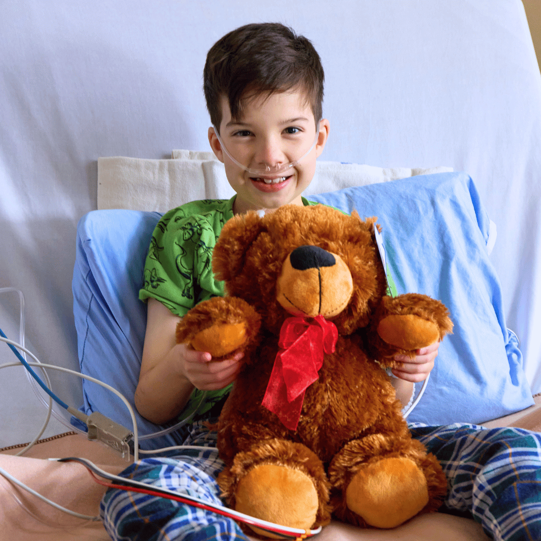 کودکی که روی تخت بیمارستان نشسته و یک خرس عروسکی را در آغوش گرفته است