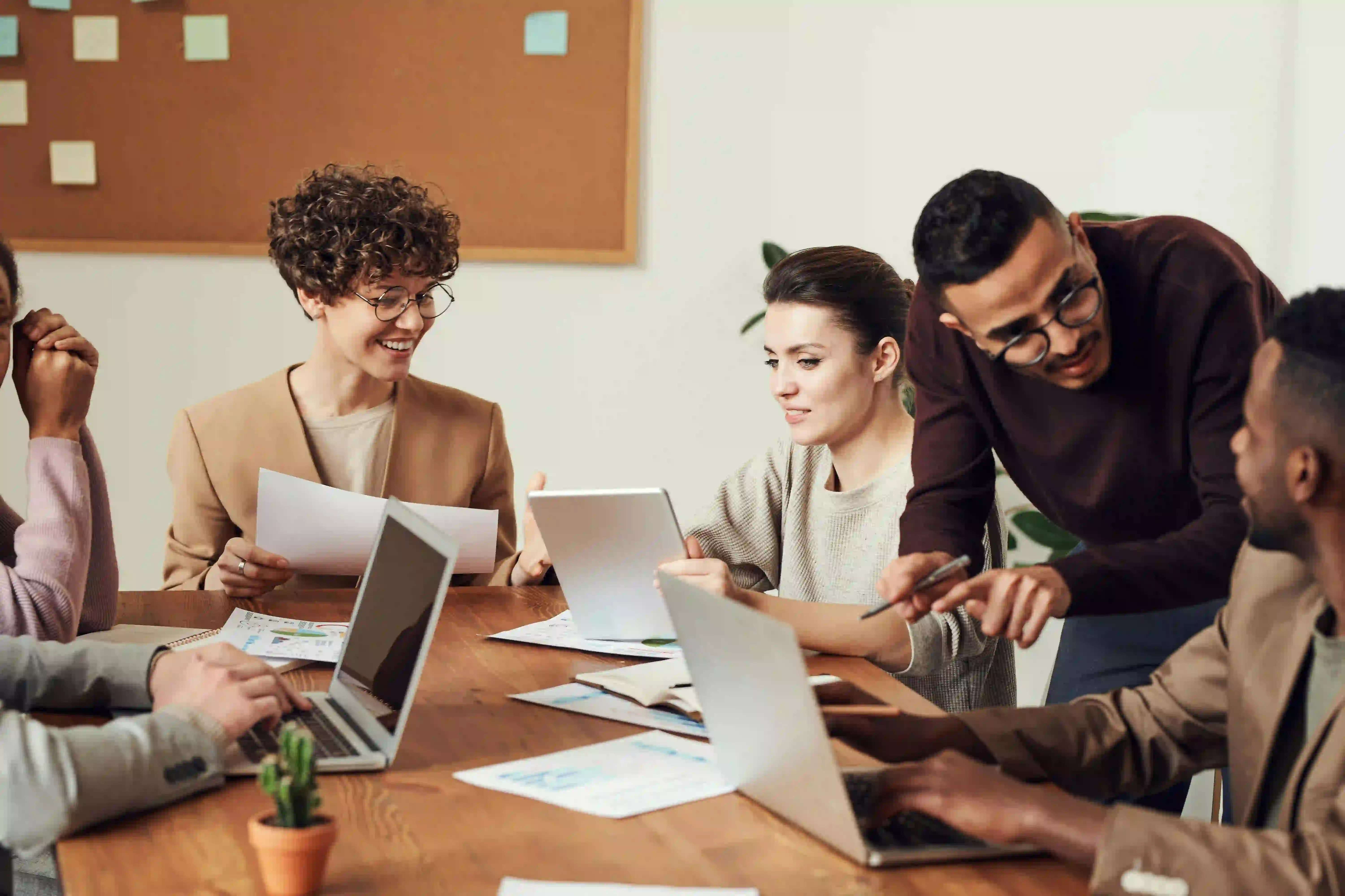 A group of people working at an office desk with laptops and documents