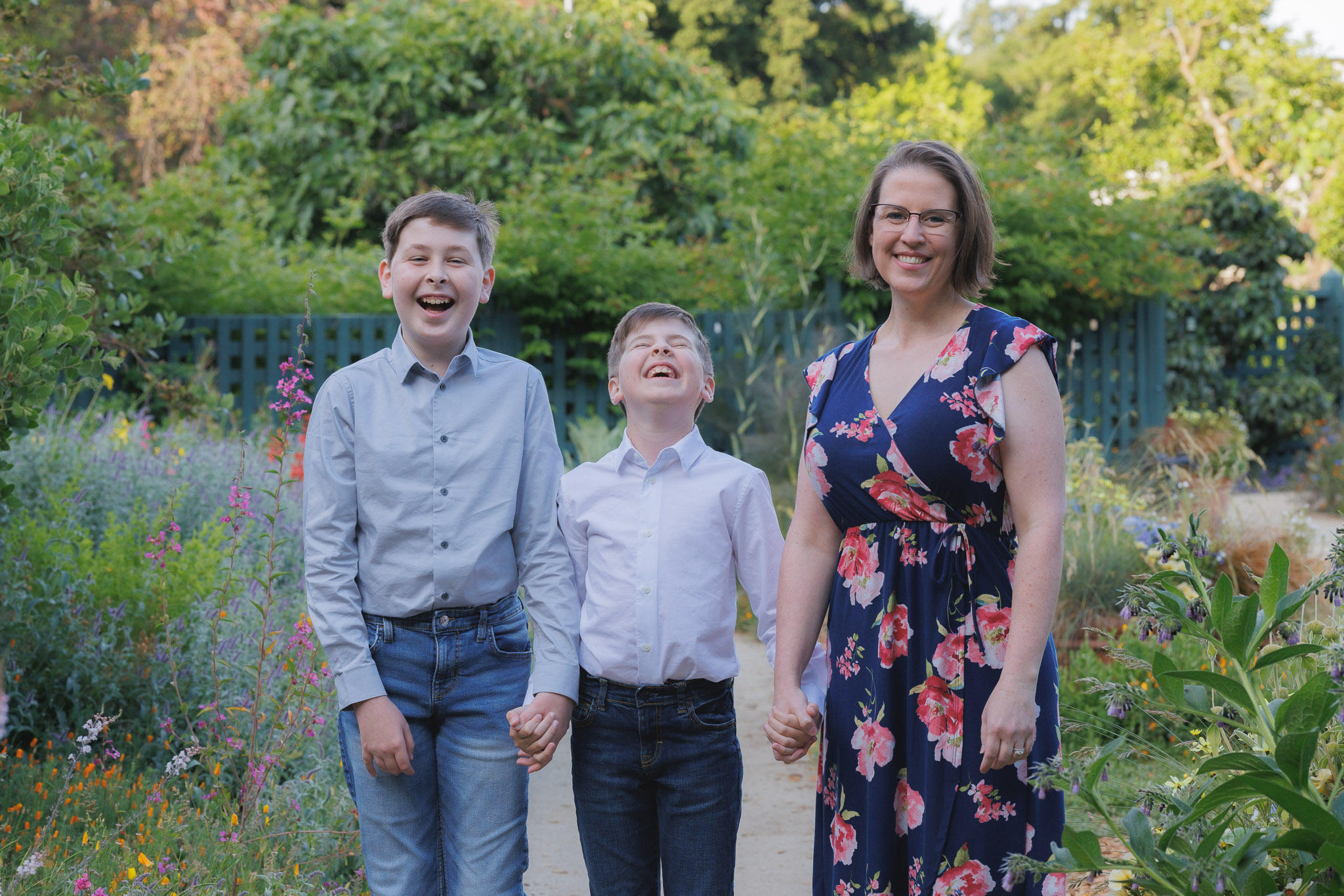 A mom and two sons holding hand and smiling at a garden photography
