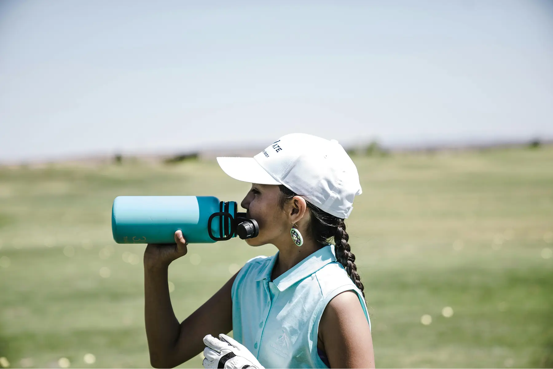 Woman drinking bottled water on a sunny day at a golf outing.