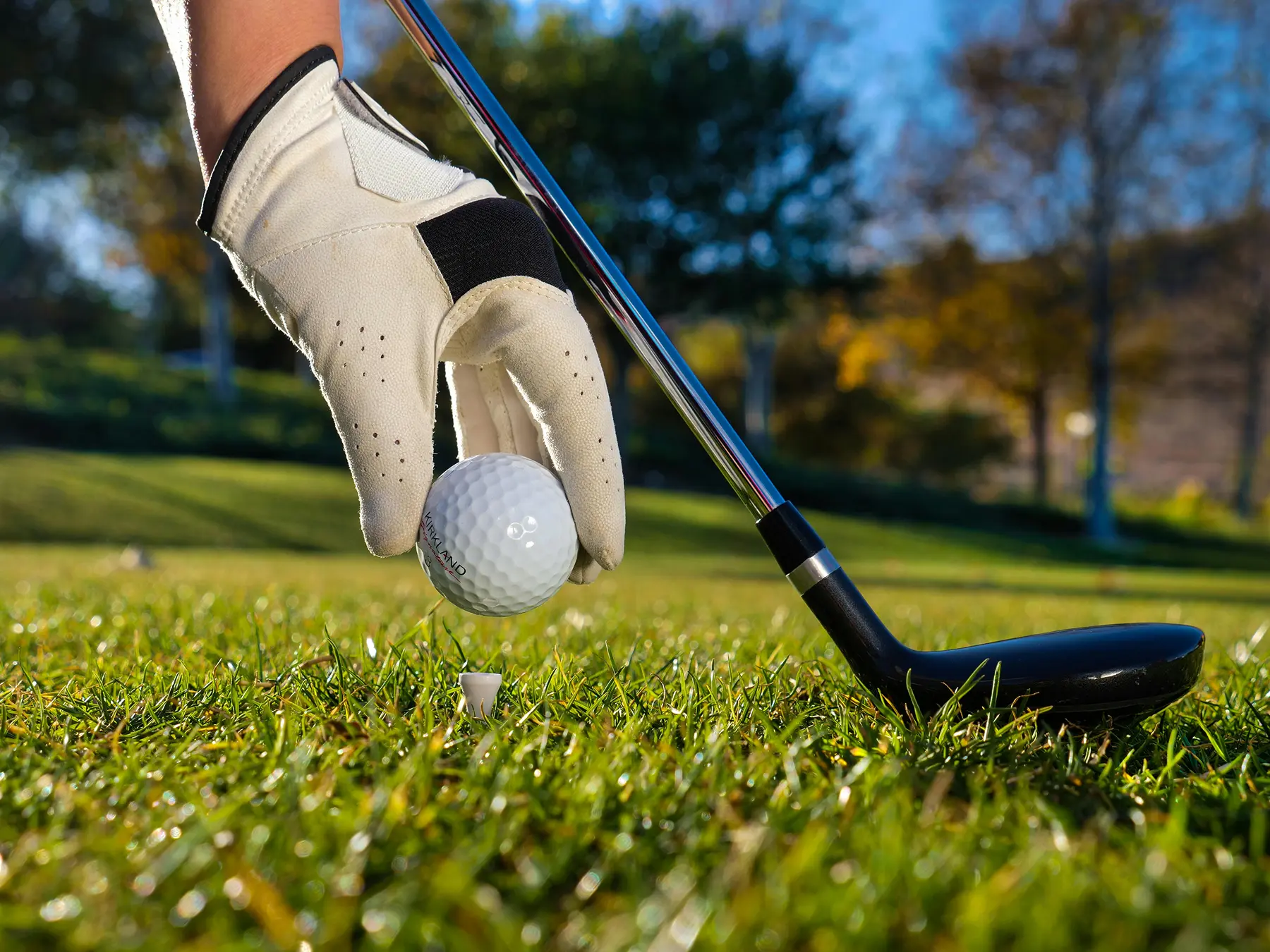 How to run a golf outing, close-up of a golfer’s hand placing a golf ball on a tee with the text prominently displayed in the foreground