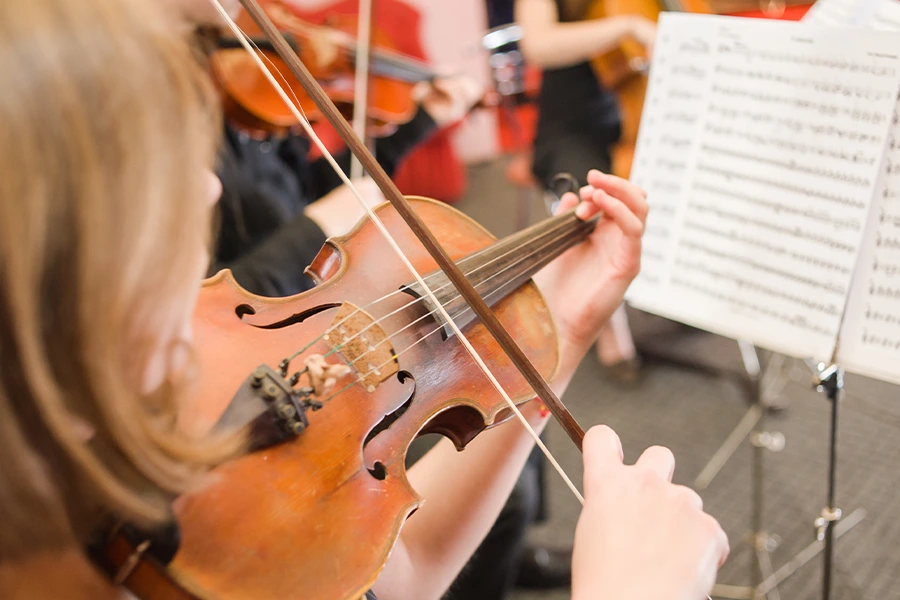 Student practicing a violin. School orchestras need performing arts fundraising to thrive.