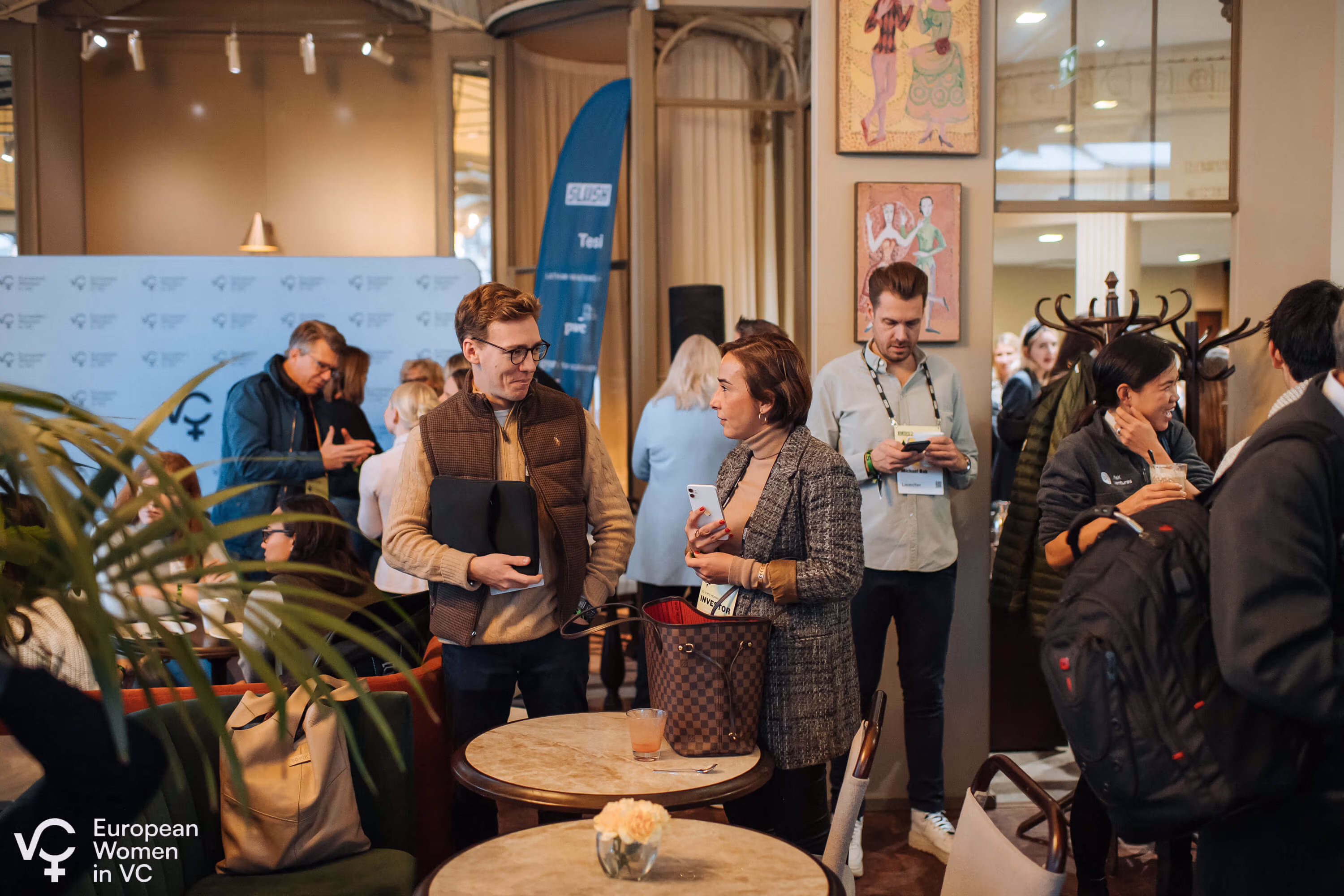 Group of professionals conversing and using phones at a European Women in VC networking event in a cozy indoor setting.
