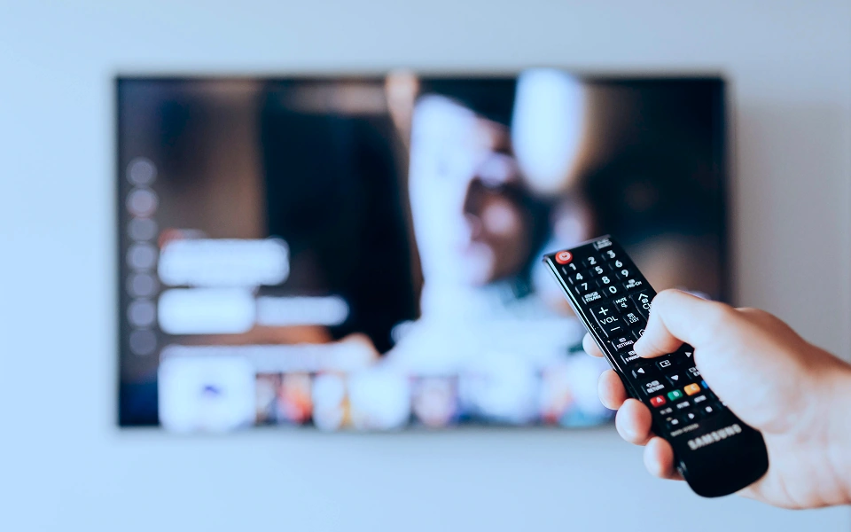Person holding a remote and pointing at a smart TV streaming platform, illustrating connected TV advertising.