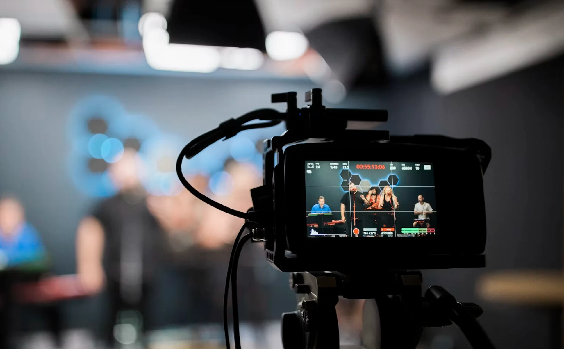 A professional camera screen displays a musical group performing live in a studio, with the actual stage blurred in the background.