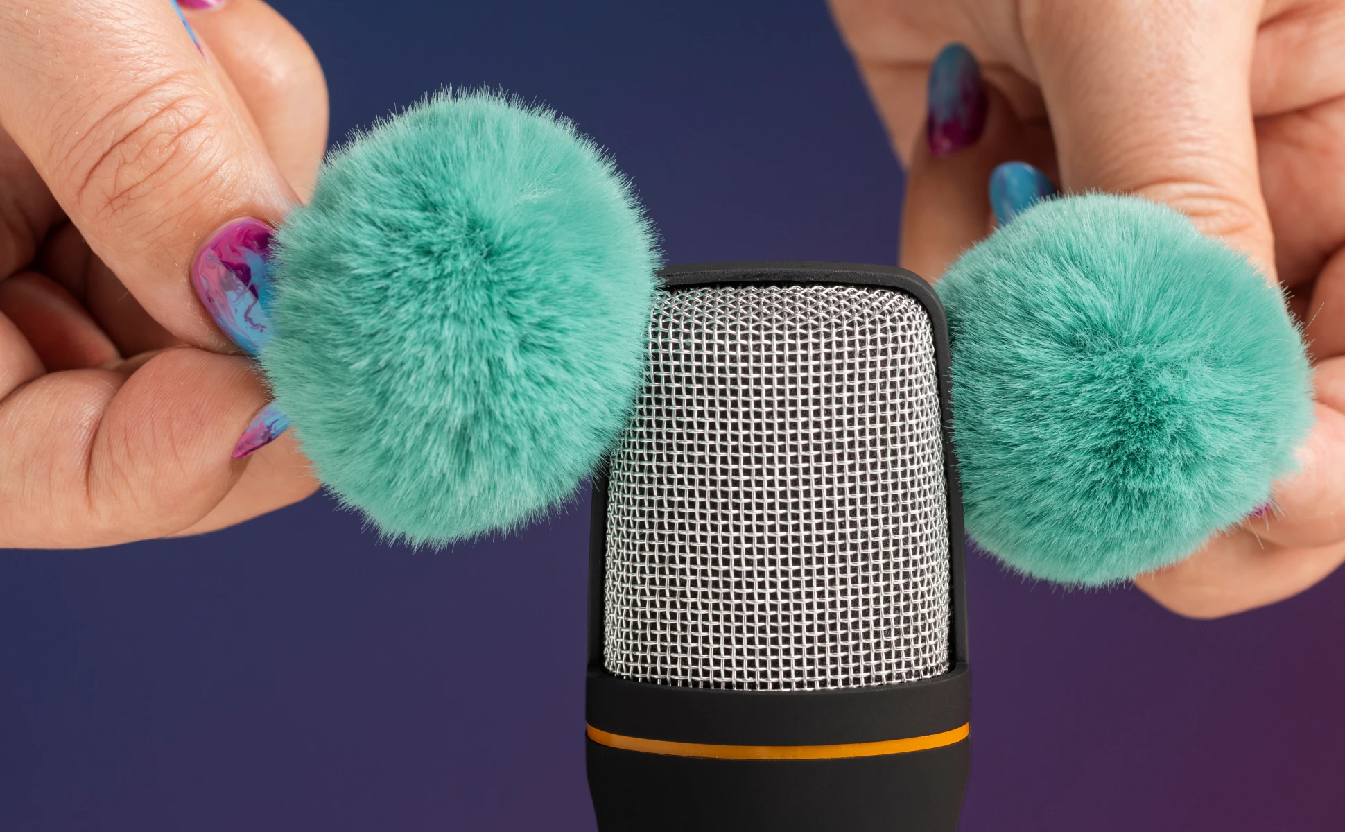 A close-up of hands holding fluffy teal pom-poms next to a black microphone mesh, creating ASMR sounds against a gradient blue and purple background.