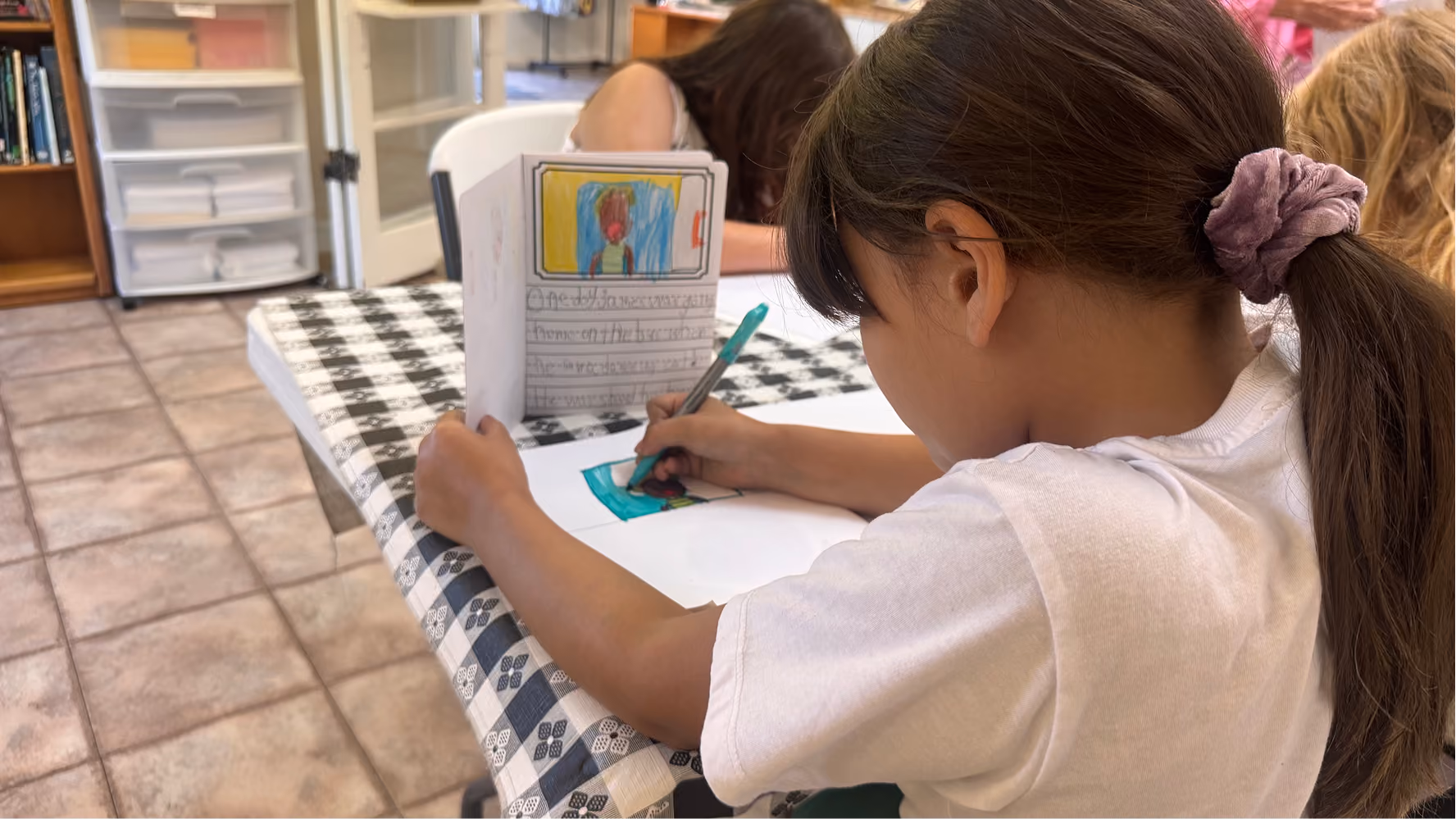 A summer camp participant colors on a sheet of paper on June 11 at the Owen County Art Guild. Girl pink hair tie.