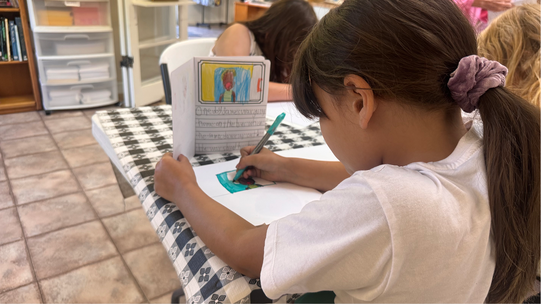 A summer camp participant colors on a sheet of paper on June 11 at the Owen County Art Guild. Girl pink hair tie.