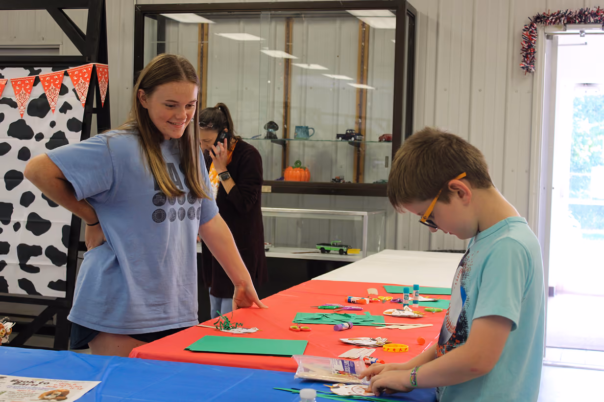 Anya DeFord watches as Winston Zigler works on a cow-themed craft at the Book 2 Barn event on July 6, 2026, at the Owen County Fairgrounds.