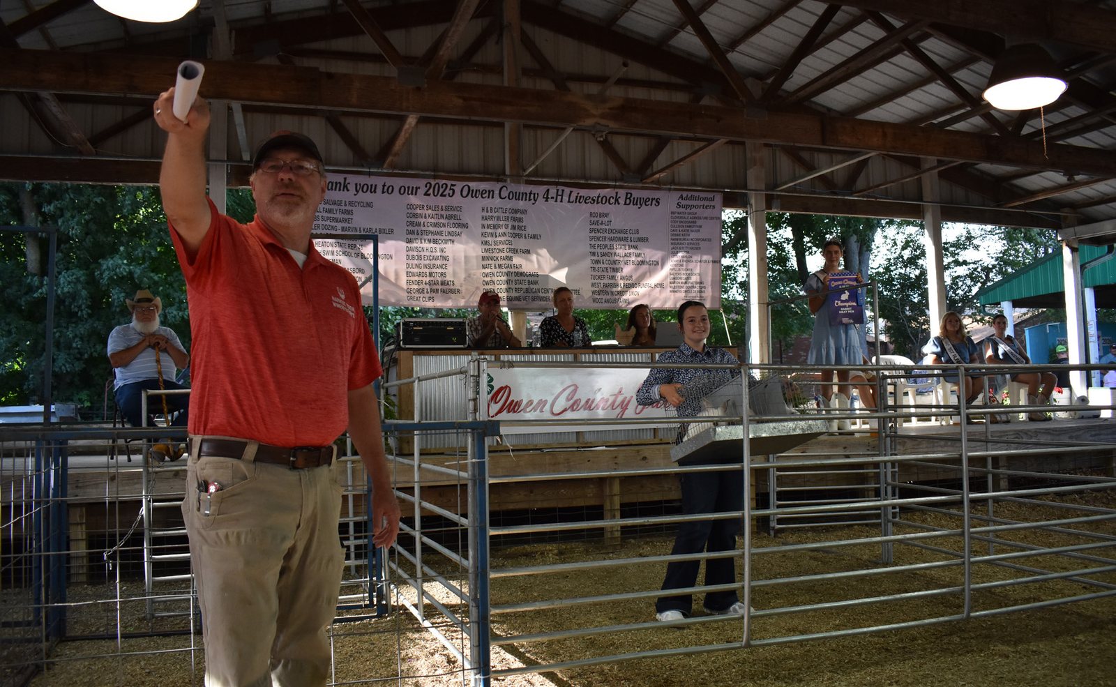 Veteran ring man Bill Williams signals a bid during the 2026 Owen County 4-H Fair Livestock Auction on July 10. In the ring, Ily Swan displays her grand champion meat pen, the auction's single rabbit entry, which was purchased by Bob Jones for $800. TRAVIS