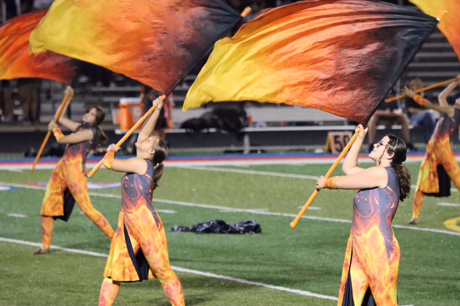 Color guard members in flame costumes wave large orange and black flags on the football field.