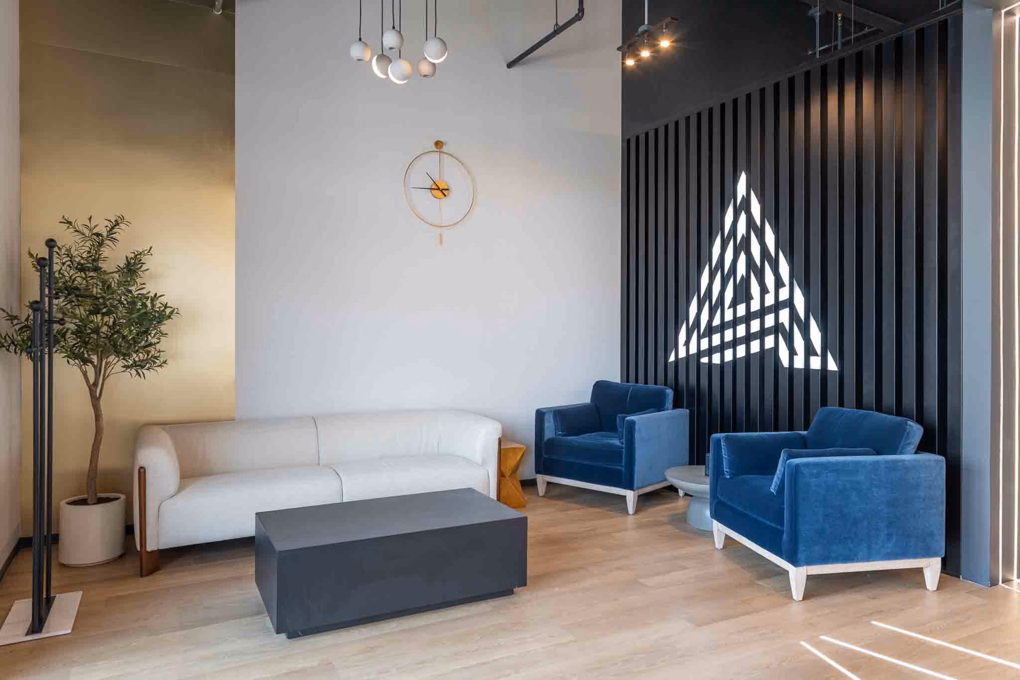 Adjusted Health + Performance waiting area with a white sofa, blue velvet chairs and lit triangle logo