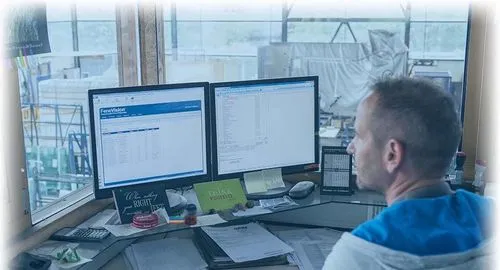 a man, sitting at a desk, viewing two computer monitors displaying Fenetech software