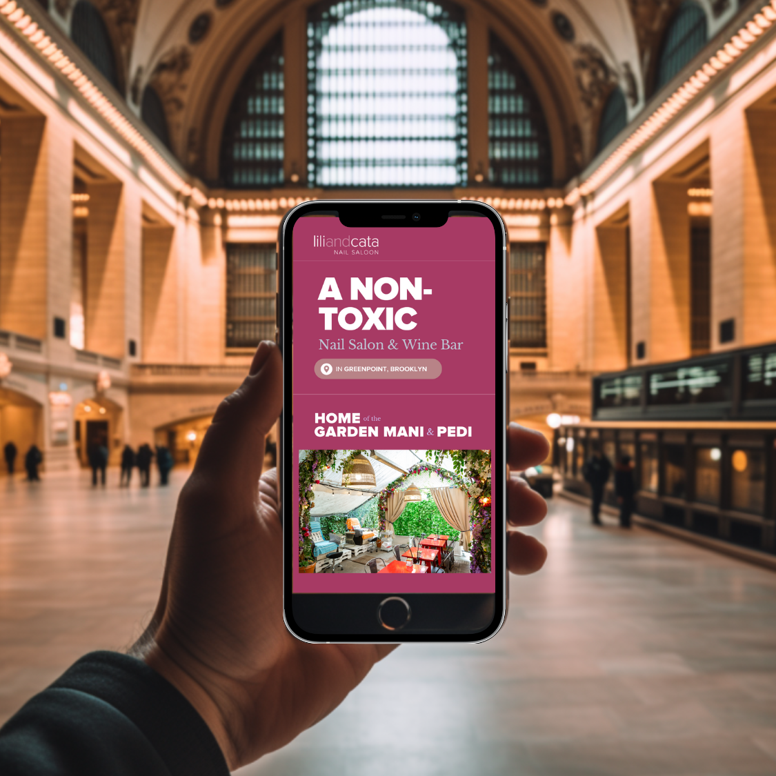 Hand holding a smartphone displaying a website for a non-toxic nail salon and wine bar in Greenpoint, Brooklyn with an image of a garden-themed manicure and pedicure area.