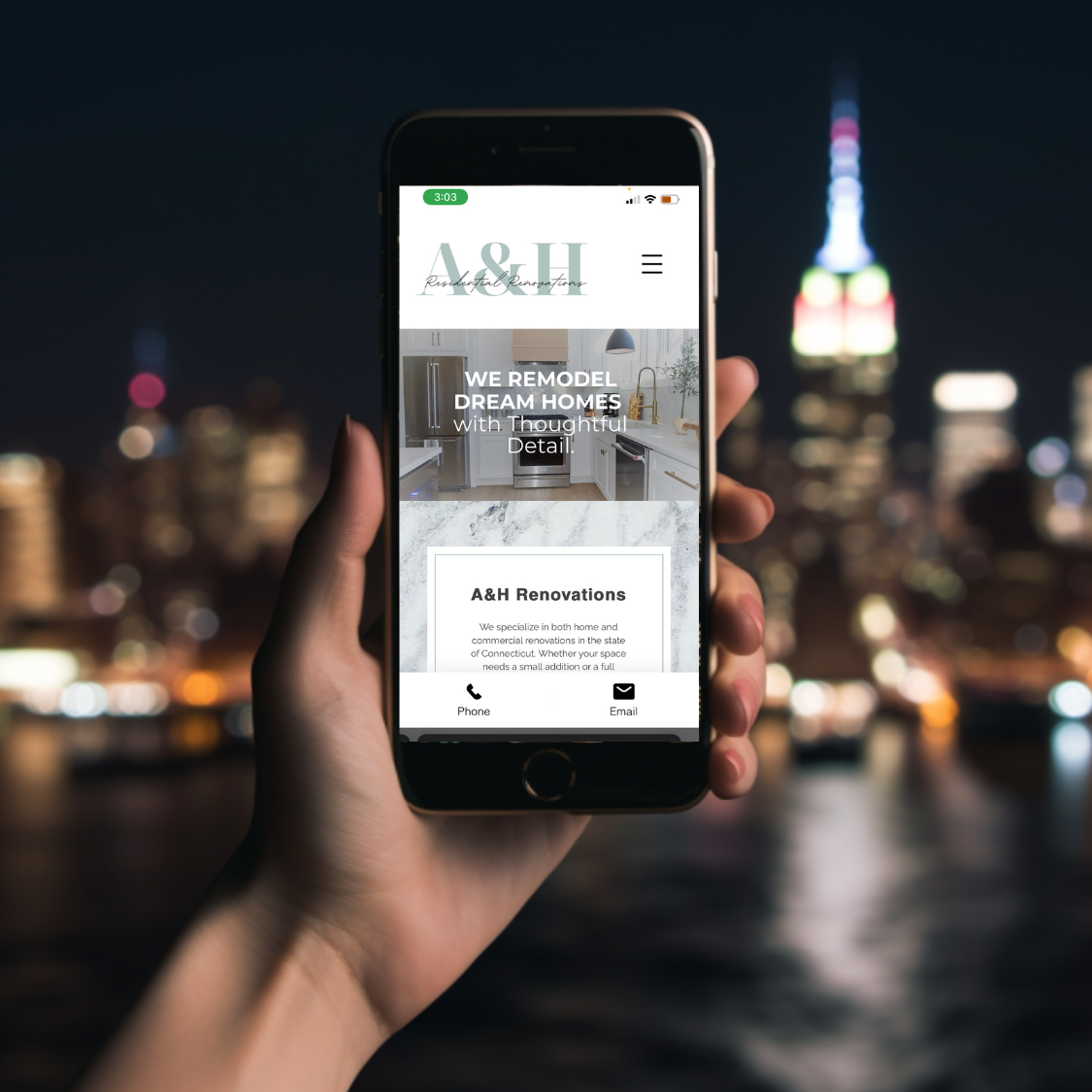 Hand holding smartphone showing A&H Renovations website with kitchen image and contact options, city skyline blurred in background.