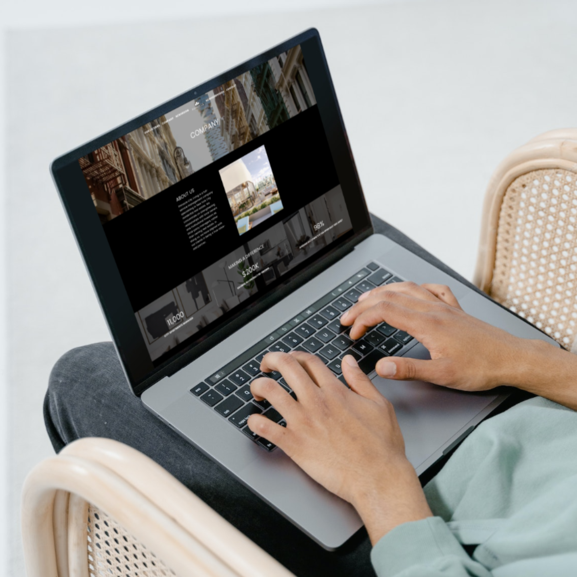 Person typing on a laptop showing a company webpage with urban building images and statistics.