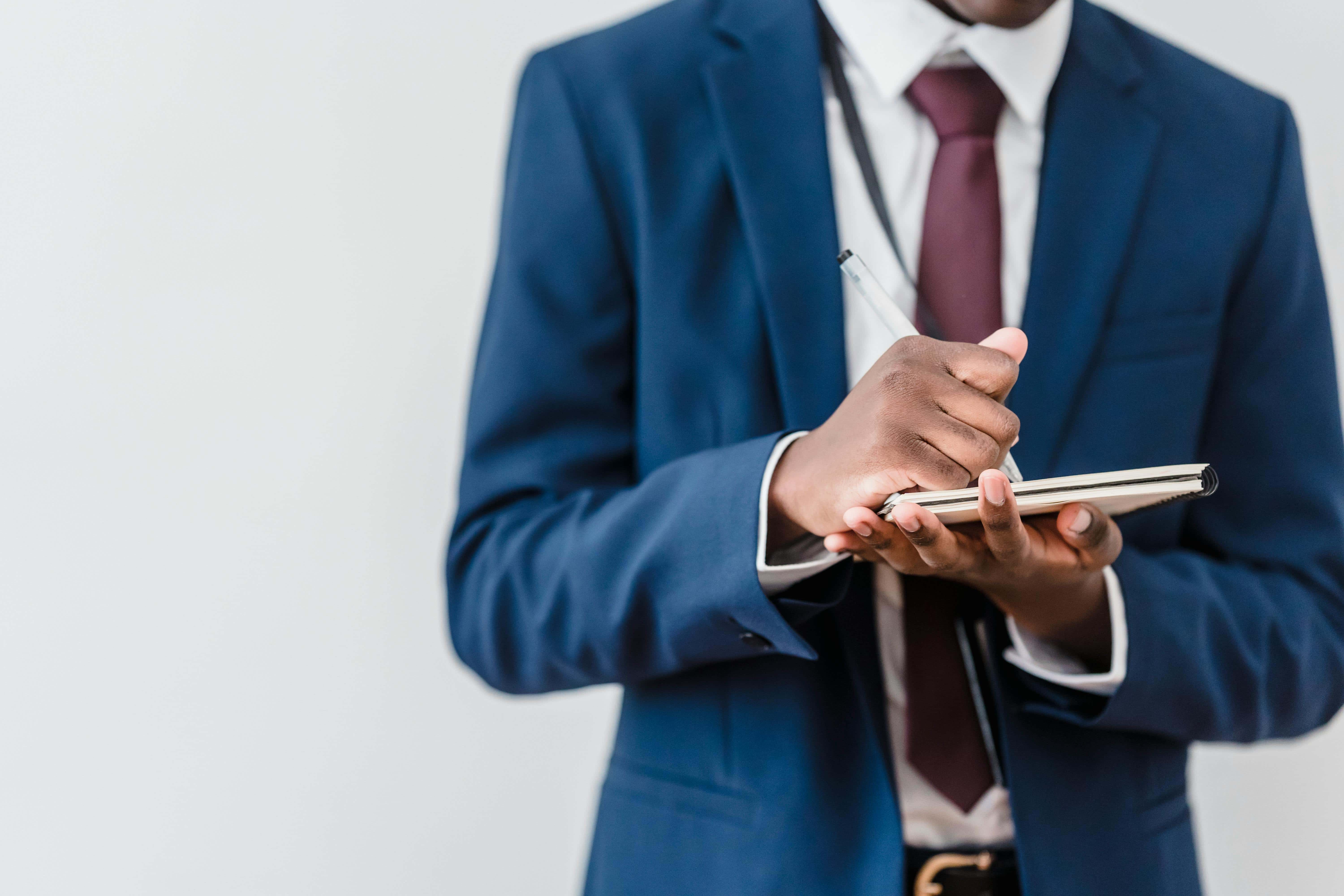 A business professional in a dark suit taking notes on a notepad during an equipment appraisal.