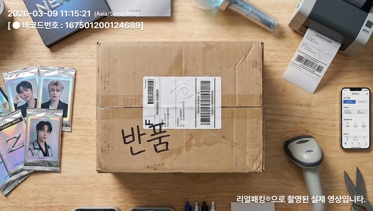 책상 위에 반품이라고 적힌 택배 상자와 K팝 포토카드, 바코드 스캐너, 라벨 프린터, 휴대폰이 놓여진 모습.