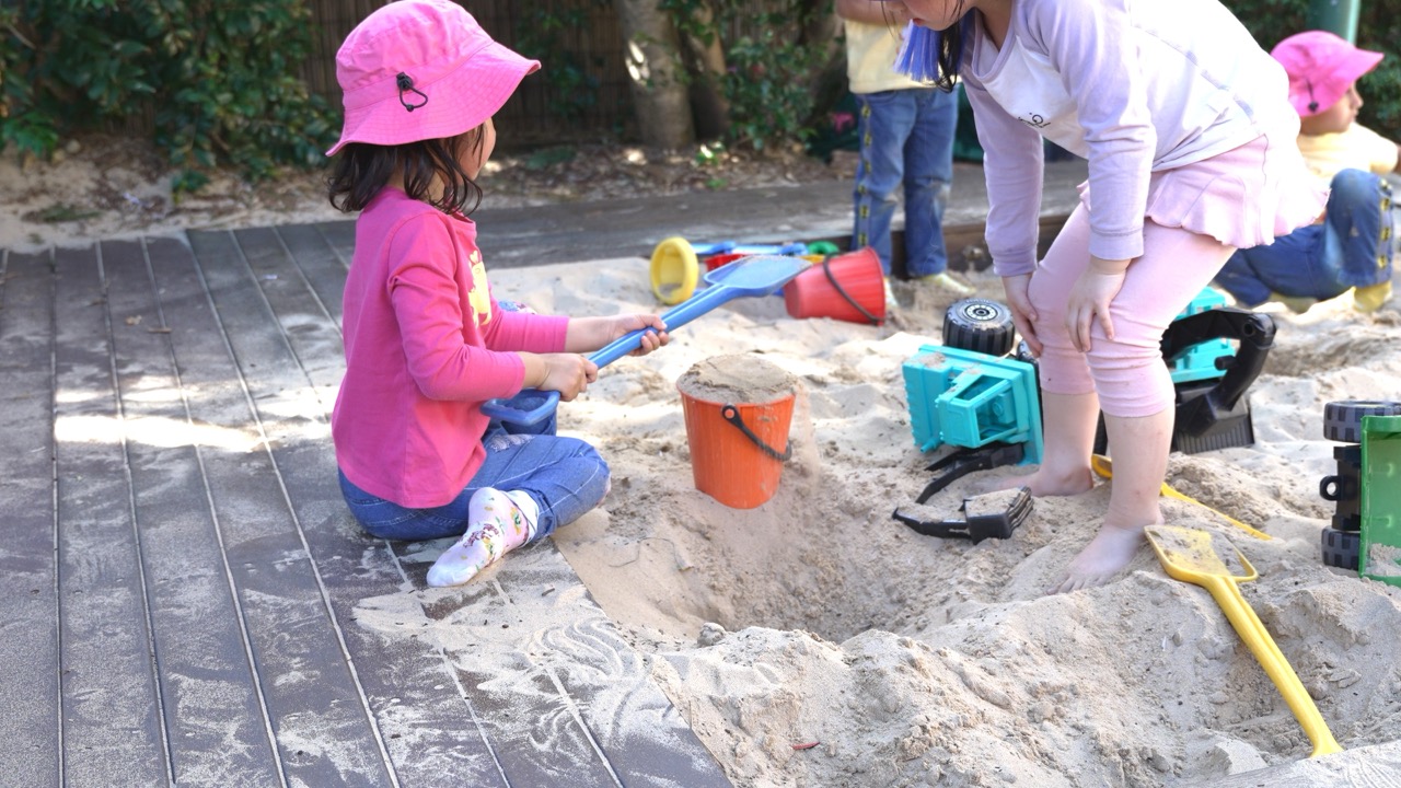 Children in sun hats digging and building in the sandpit