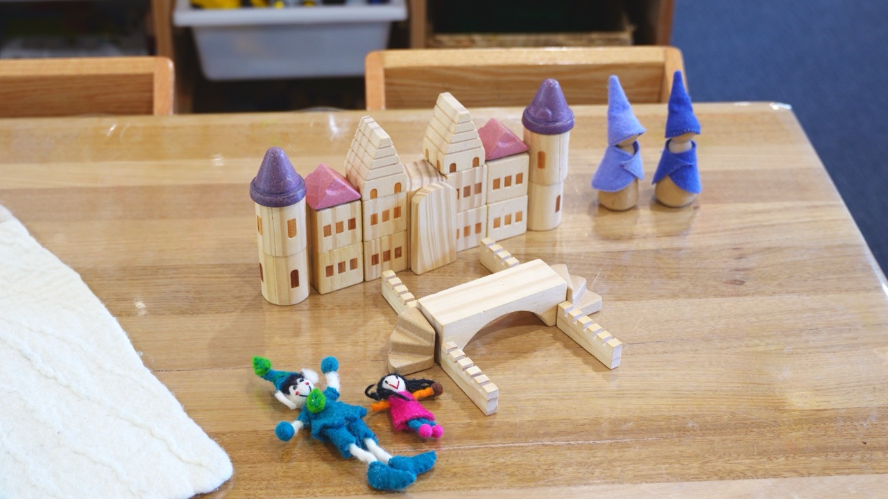 Wooden castle blocks and peg dolls set up on a table for imaginative play