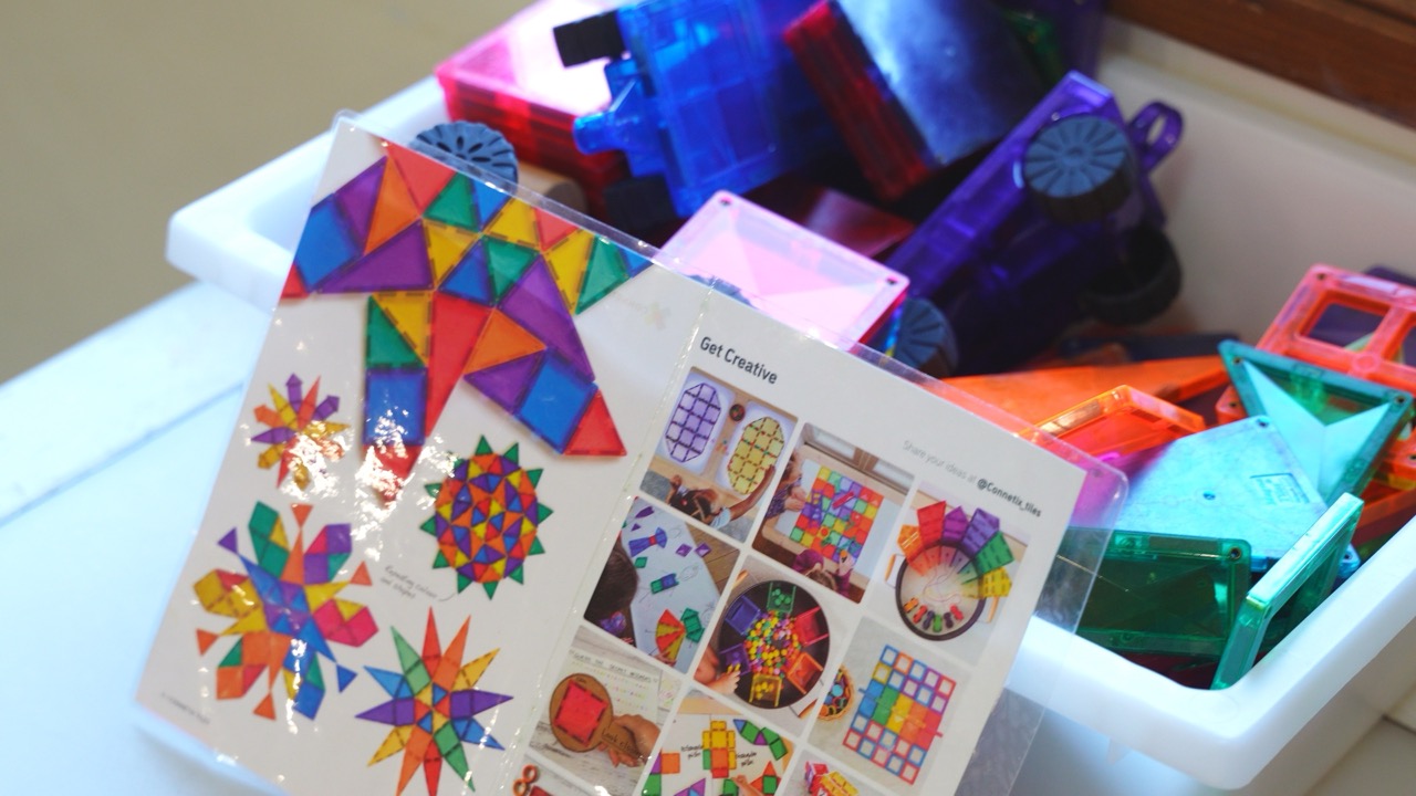 Tub of colourful magnetic tiles with a pattern card for building and design