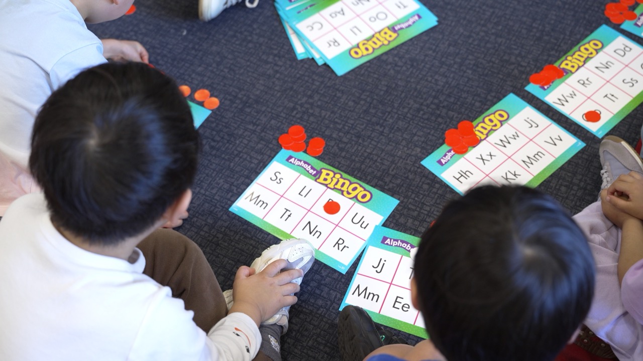 Preschoolers playing alphabet bingo on the mat to practise their letters