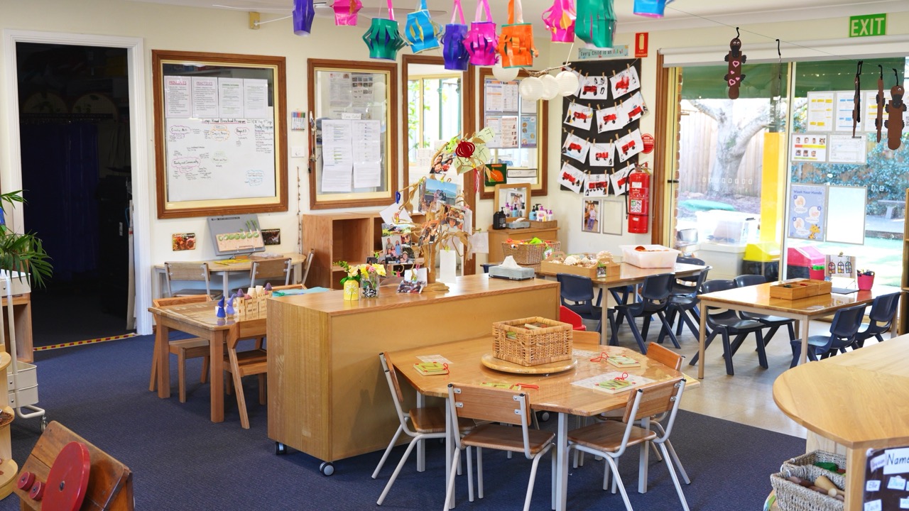 Preschool room with child-sized tables and chairs, open shelves and doors to the garden