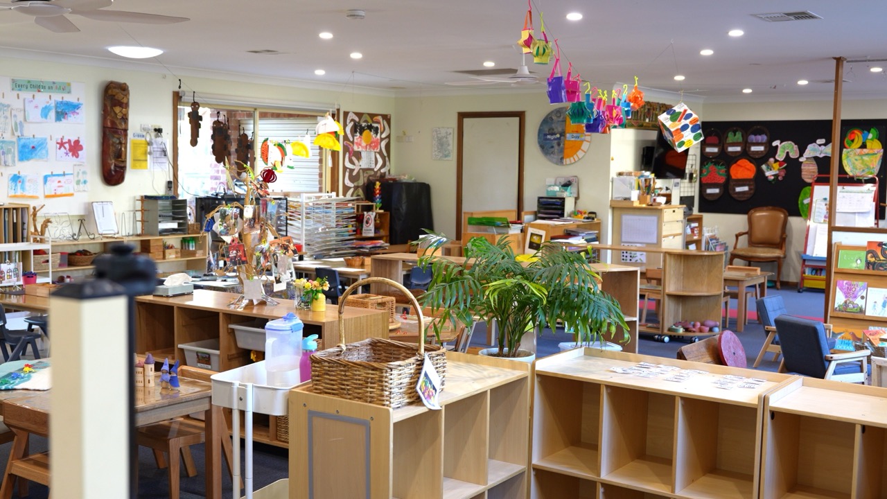 Bright preschool playroom with low wooden shelves, plants and children's artwork