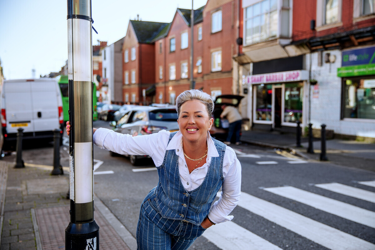 Woman smiling and hanging from a lamp post on the street