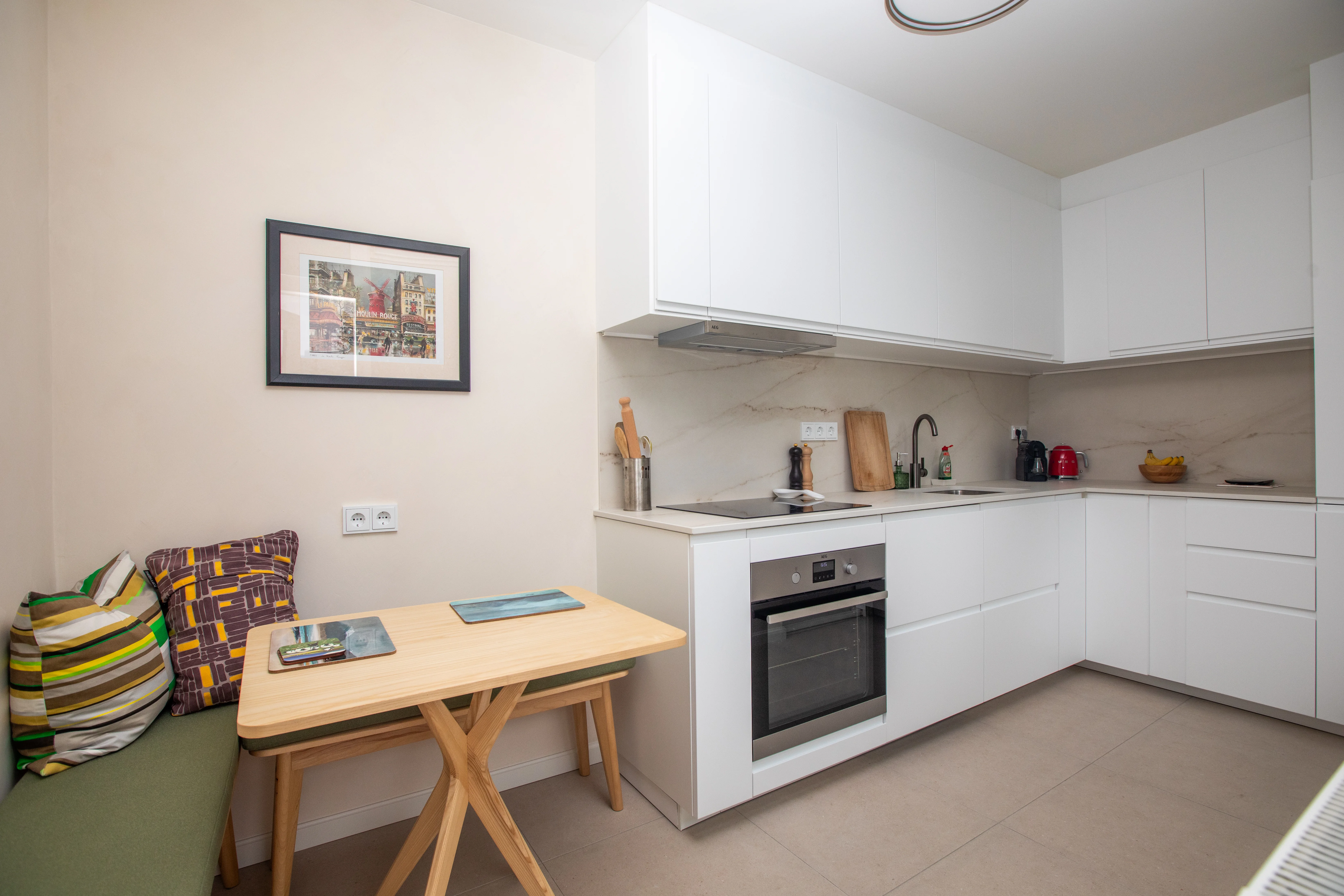 Moderne keuken met witmeubels, ingebouwde oven, houten tafel en groene bank met kussens.
