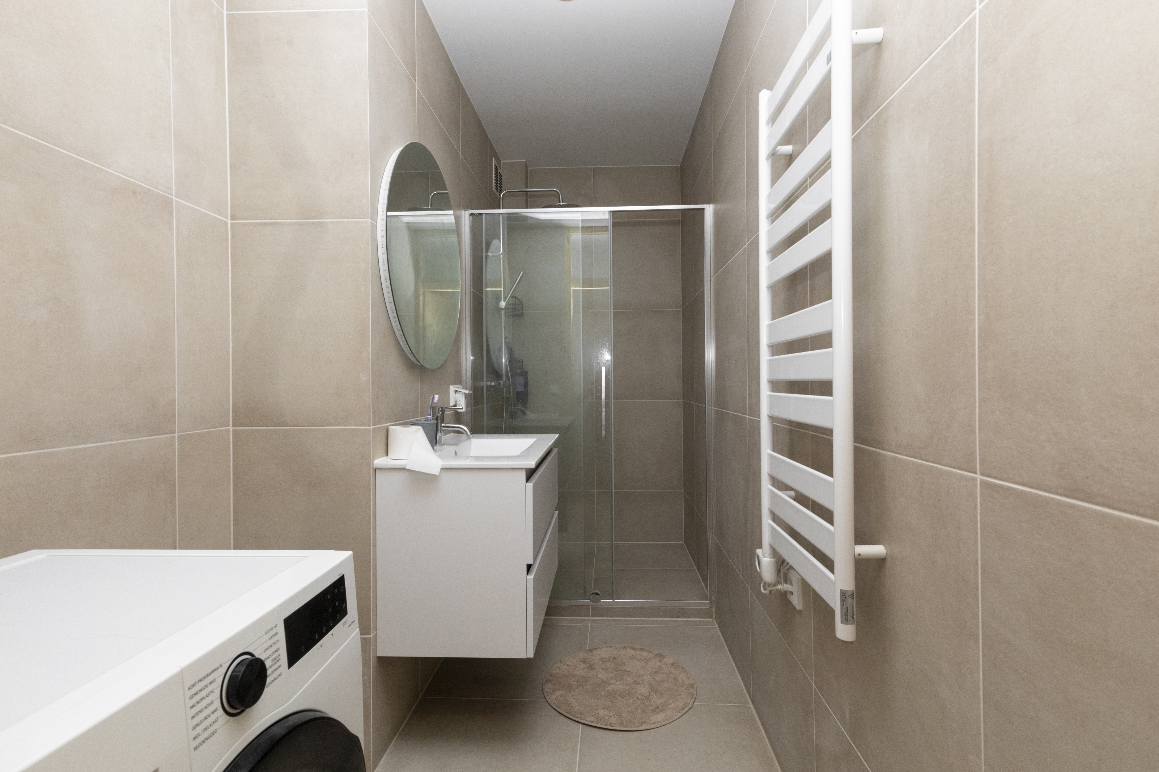Moderne badkamer met douchecabine, zwevende wastafel, wasmachine en handdoekradiator.