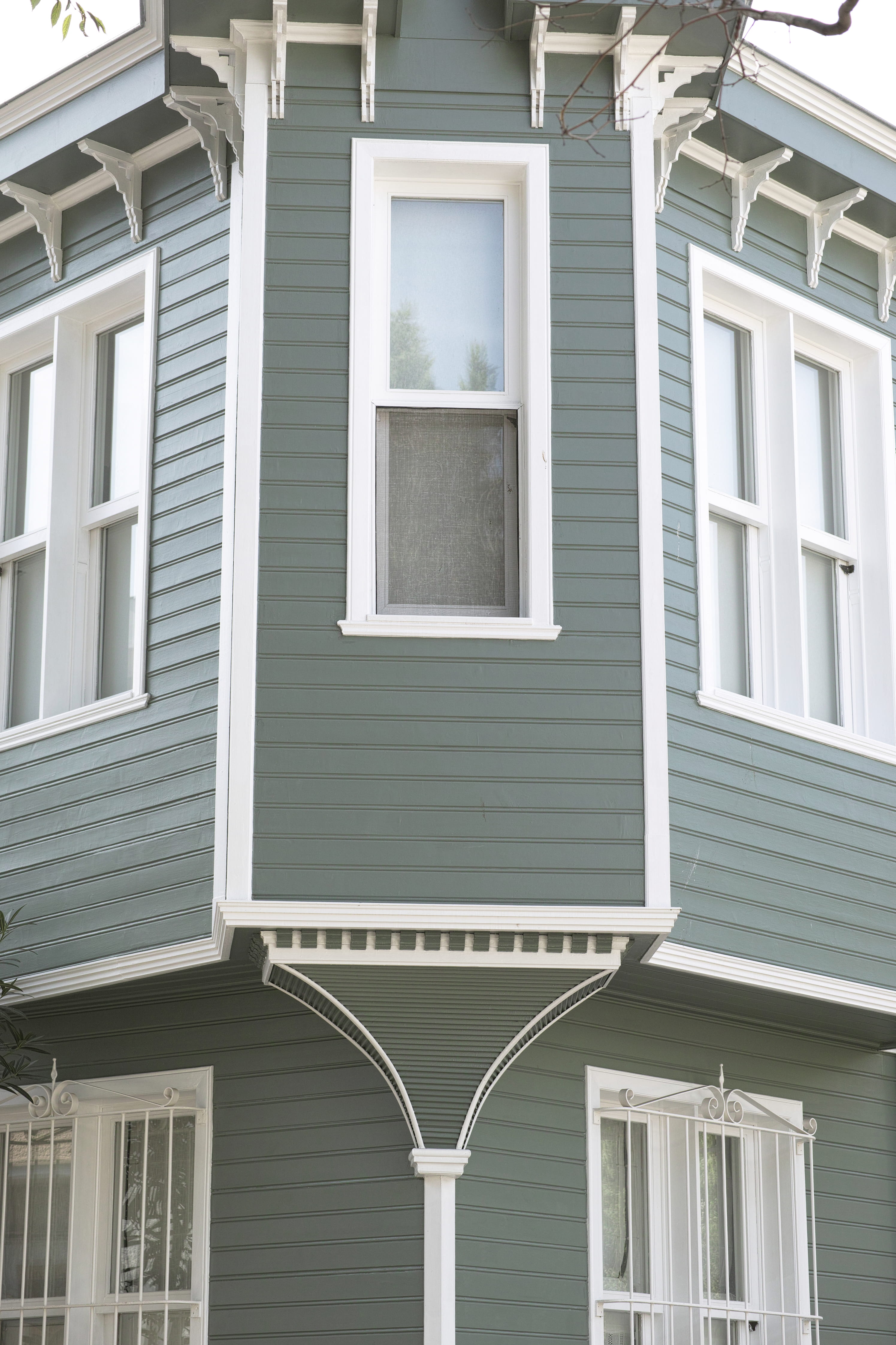 Groene gevel van traditioneel huis met witte ramen en decoratieve details.