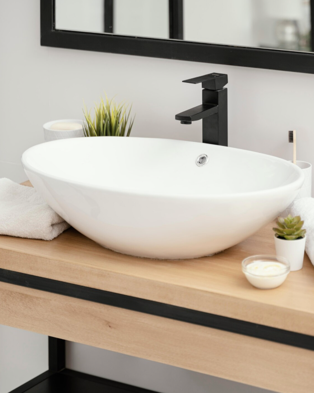 Moderne witte wastafel met zwarte kraan, handdoek en planten op houten badkamermeubel.