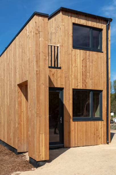 Moderne minimalistische tiny house met houten gevel, zwarte ramen en deur onder blauwe lucht.