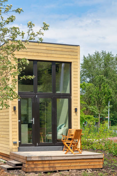Klein houten huis met grote glazen deur en twee houten stoelen op een verhoogd terras.