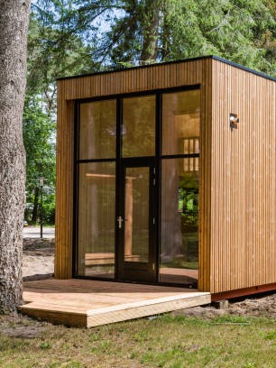 Modern klein huis met grote glazen deuren in een natuurlijke bosomgeving.