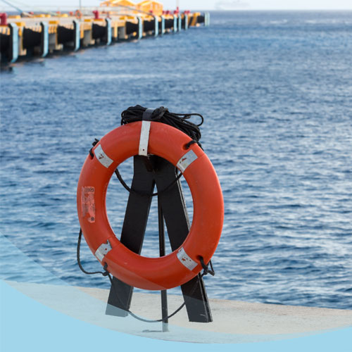 A life preserver on a stand by the water with a long pier in the background