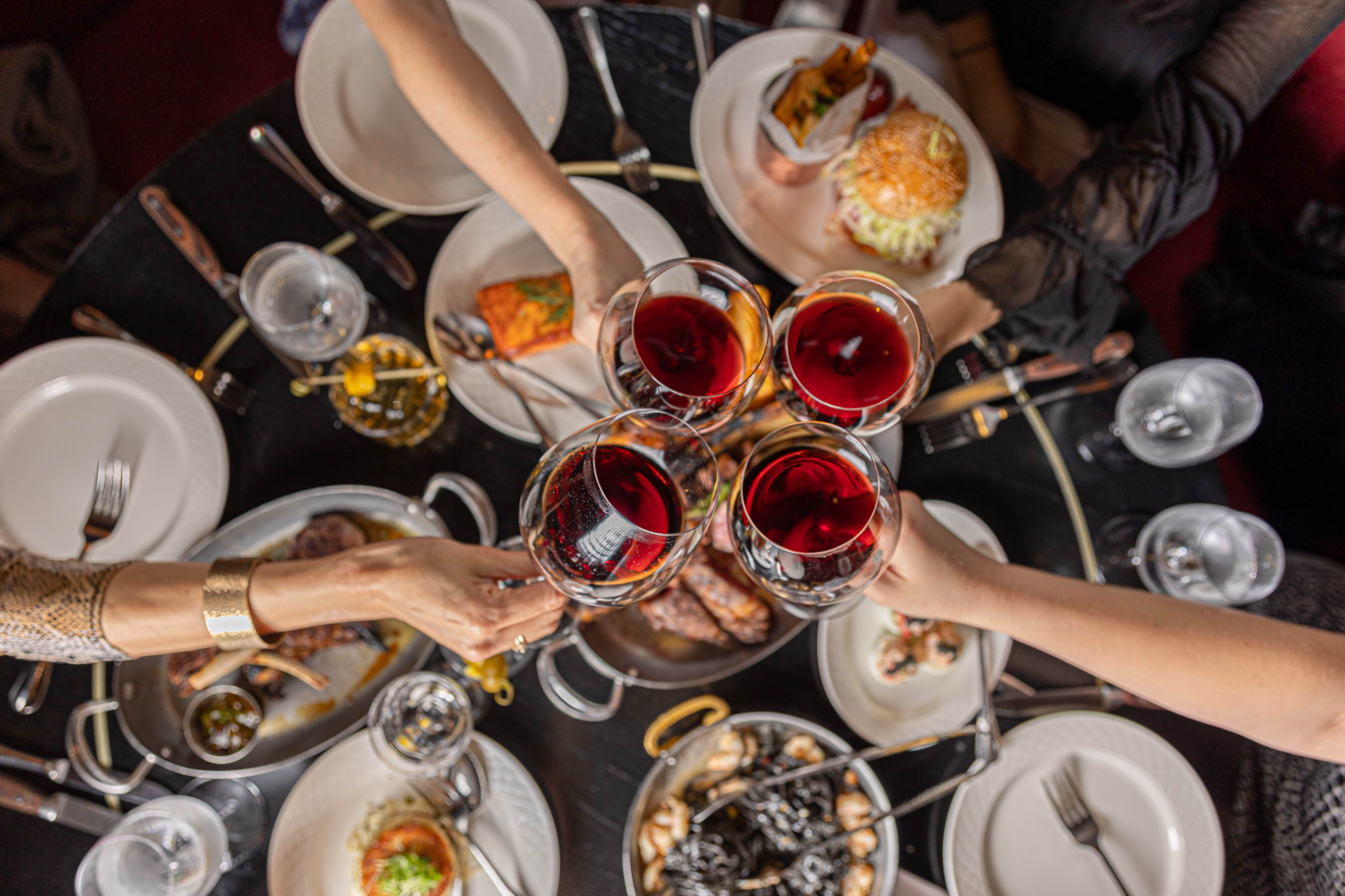 A group of people cheersing with red wine over a full table of dinner at Harry's in New York City.