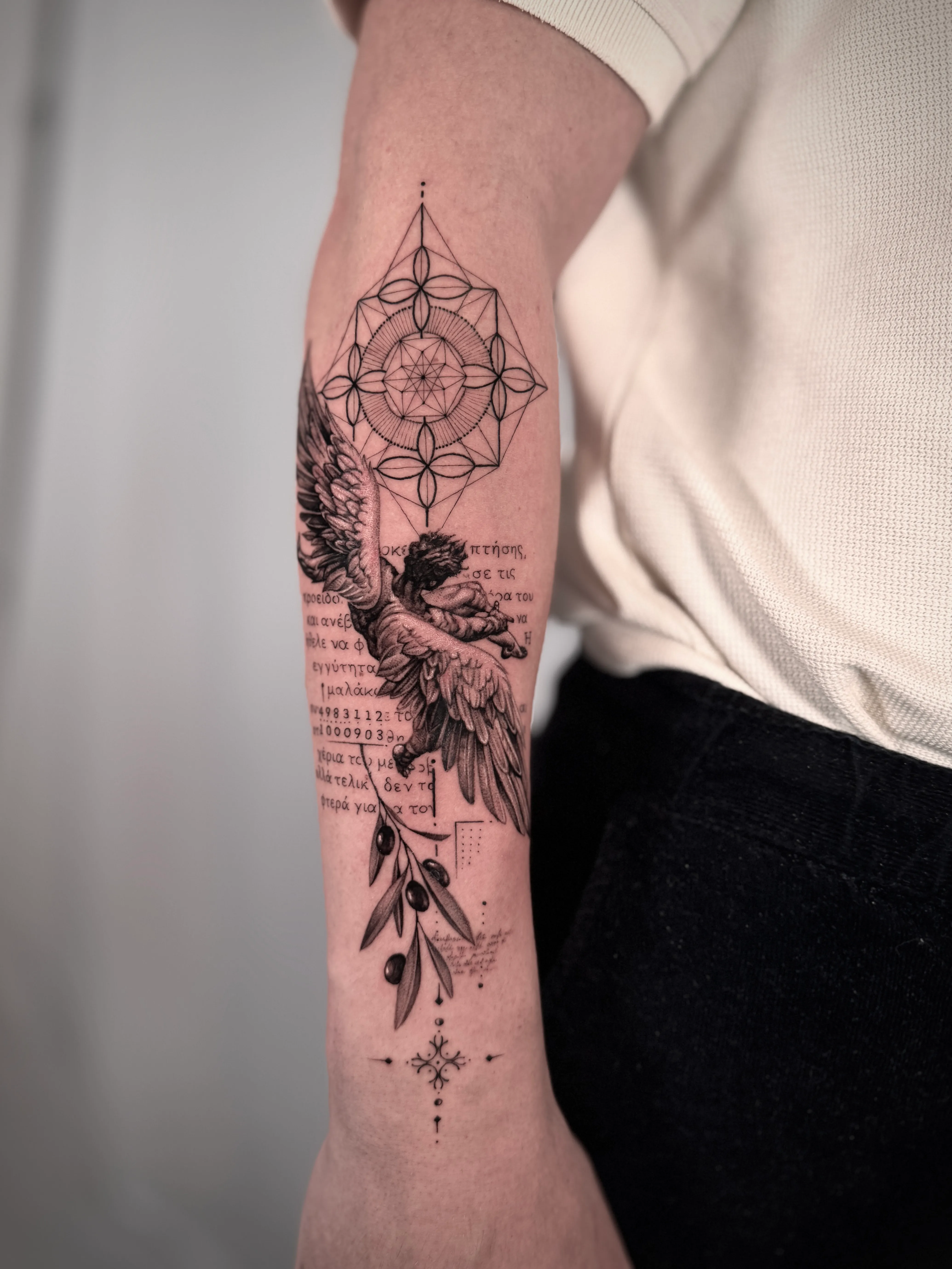 Realistisches Tattoo eines fliegenden Engels mit Flügeln und einem Olivenzweig auf dem Unterarm, umgeben von geometrischen Mustern und kursive Schriftzeichen.