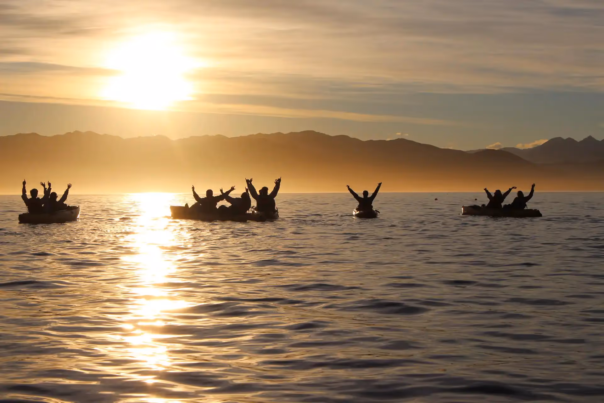 A group of people on kayaks with the sun setting behind them