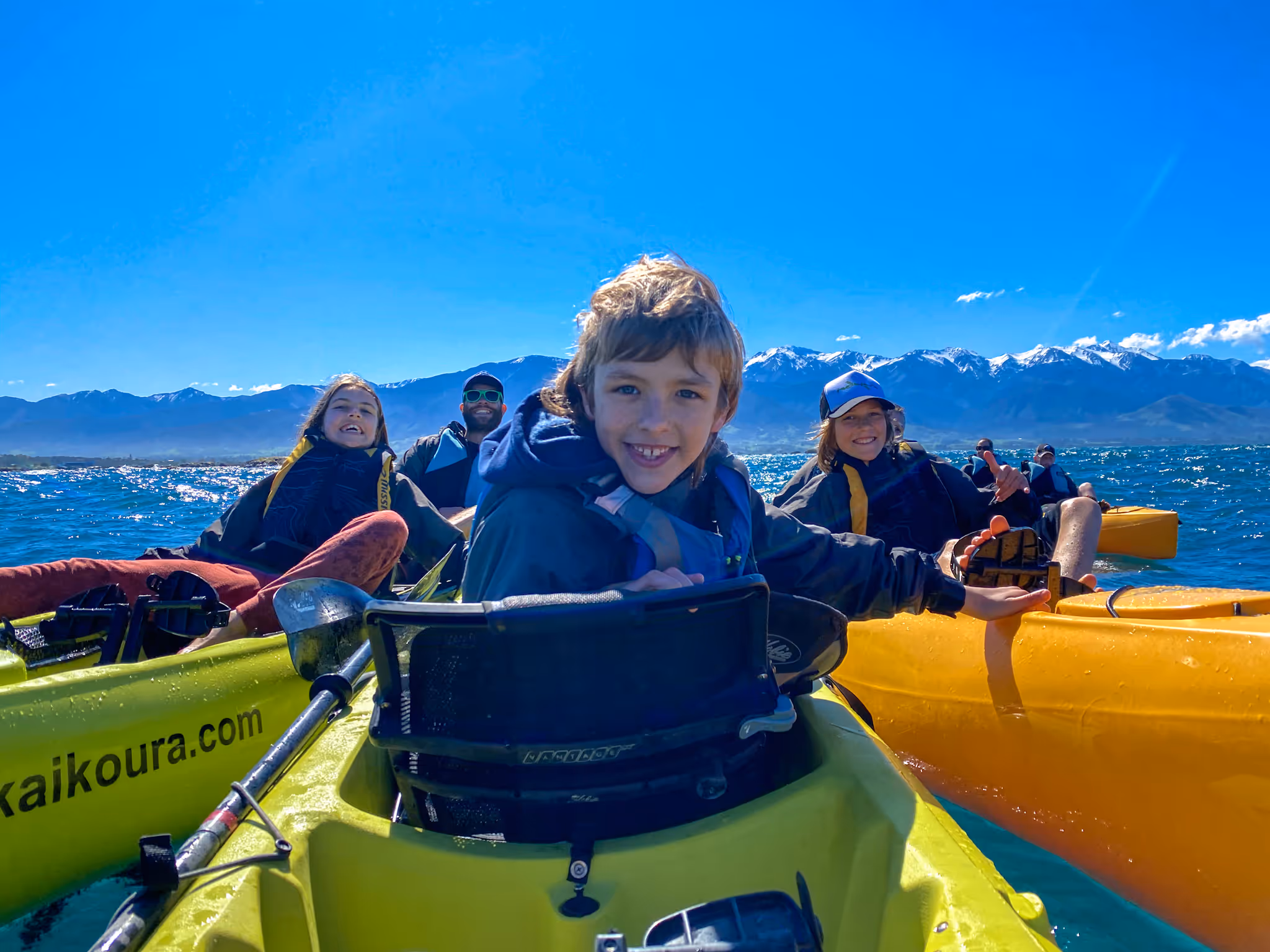 3 adults and 3 kids on pedal kayaks in Kaikoura with the snow capped mountains in the background-seals