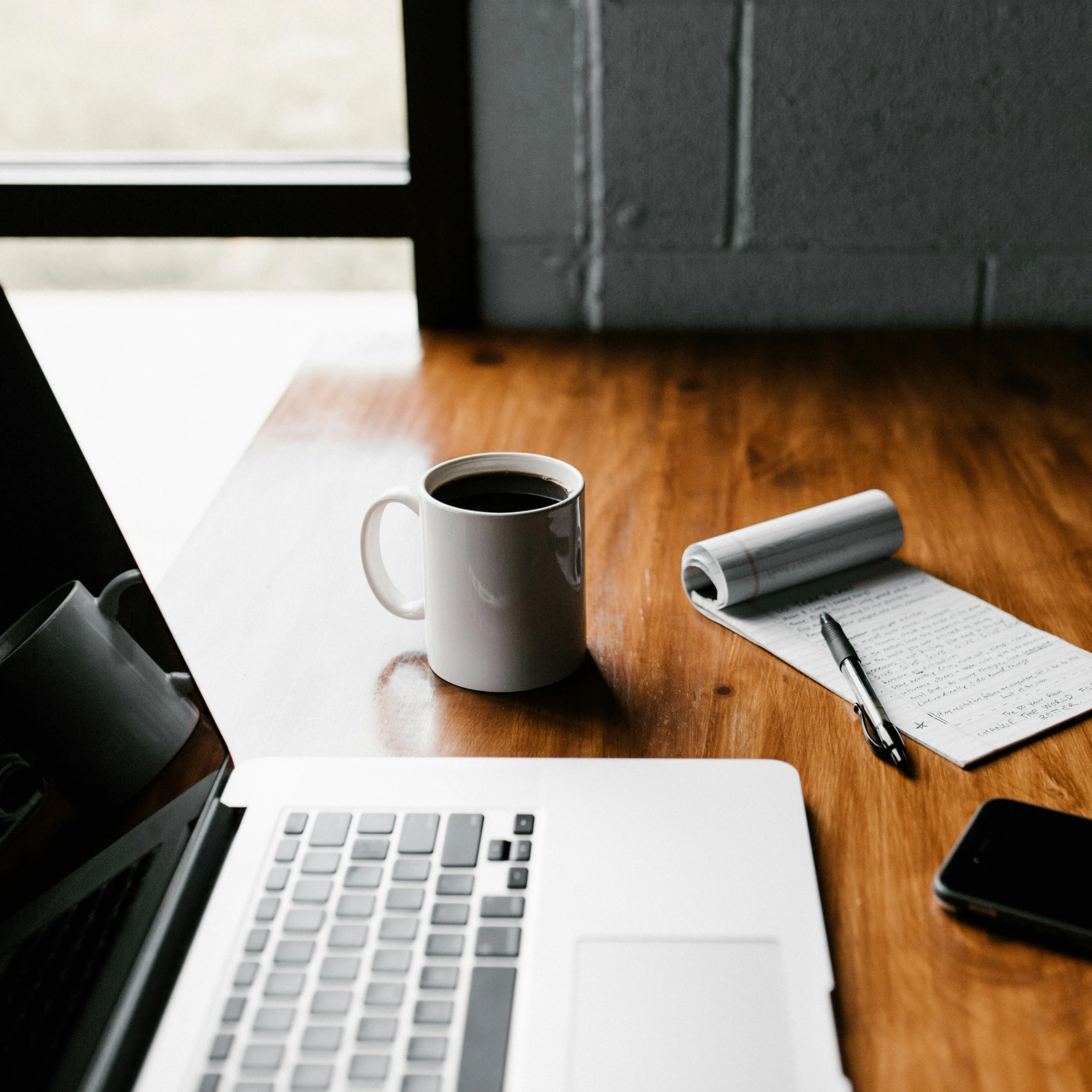 A laptop, a cup of coffe, and a note pad with a pencil over a desk