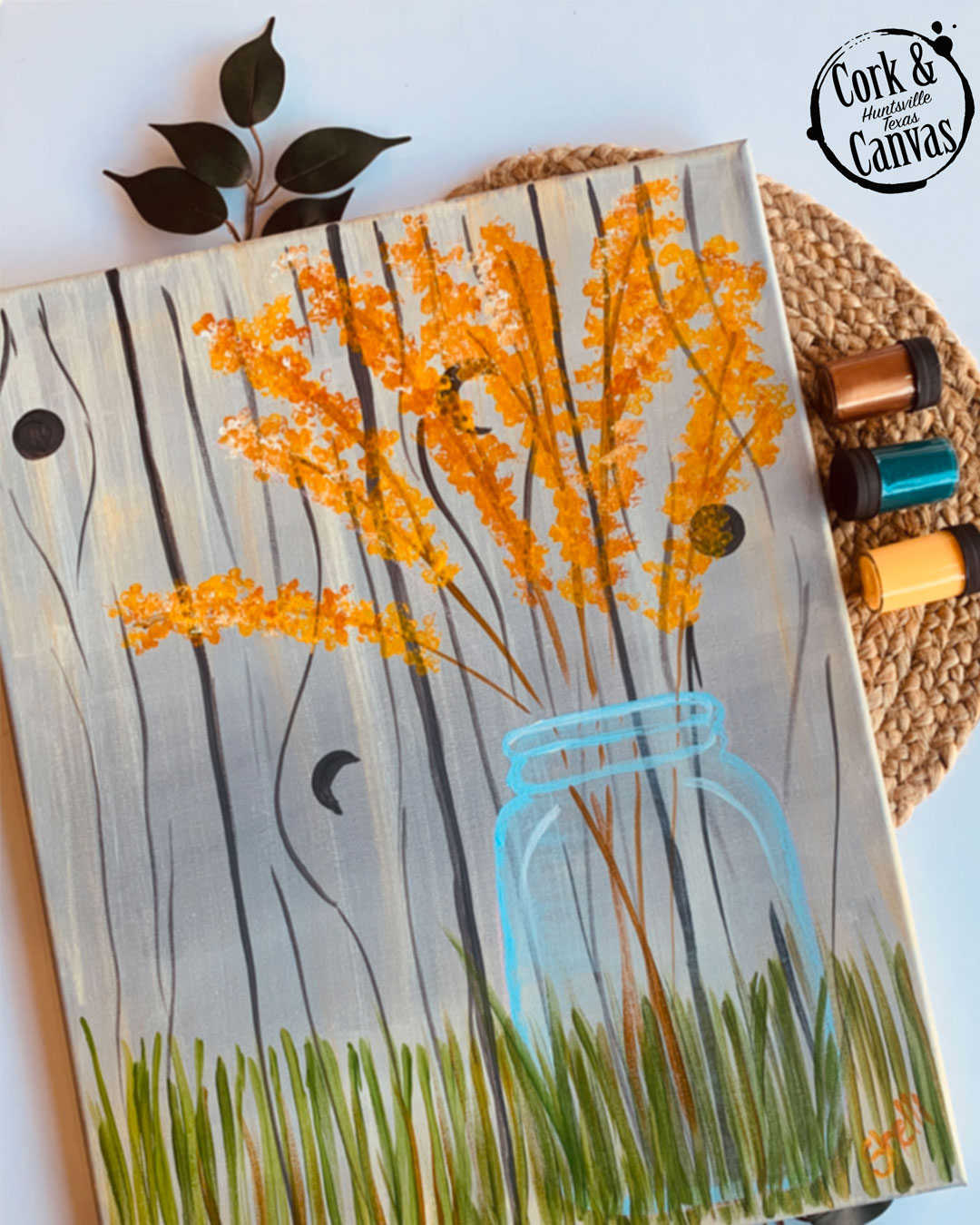 Painting of orange flowers in a blue mason jar with green grass on a wood plank background.