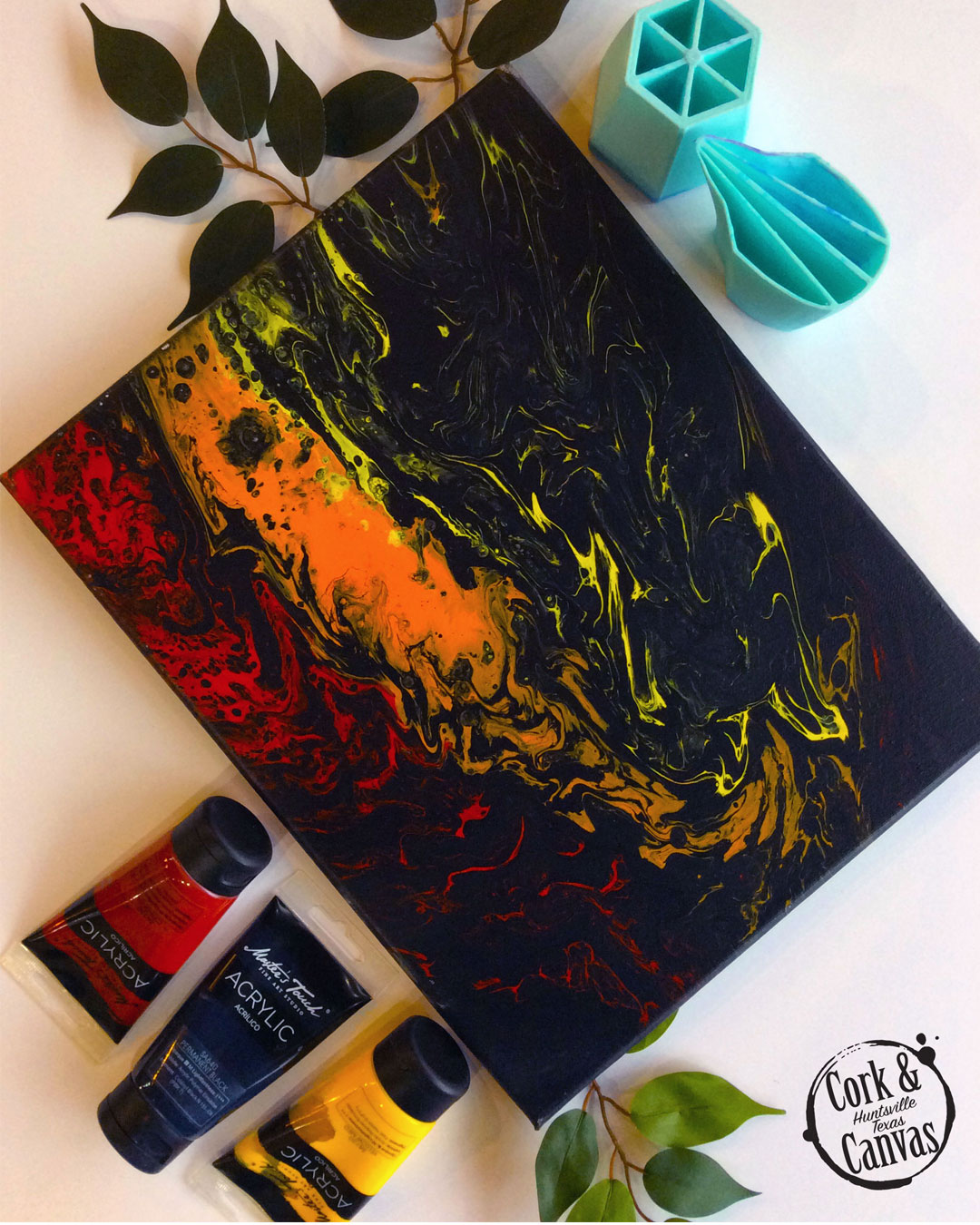 Abstract black canvas with red, orange, and yellow acrylic paint tubes and green leaves.