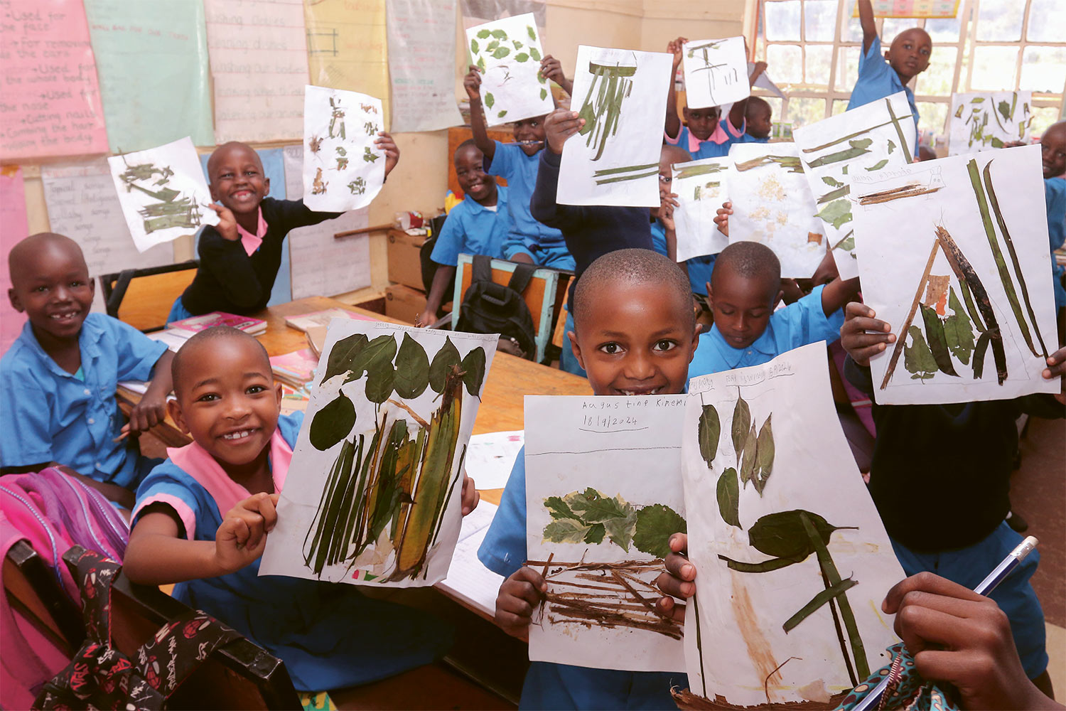 Kinder einer Schule in Kibagare, zeigen stolz ihre Kunstwerke, die aus einer Collage aus Blättern bestehen.