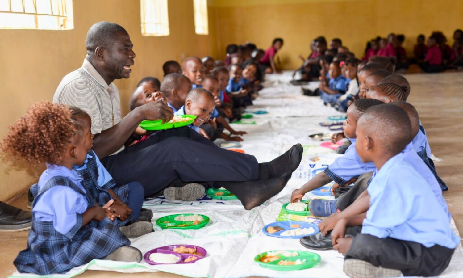Pater Daniel, Schulleiter der Maria Regina Schule in Sambia, bringt Kinder beim gemeinsamen Essen zum Lachen.