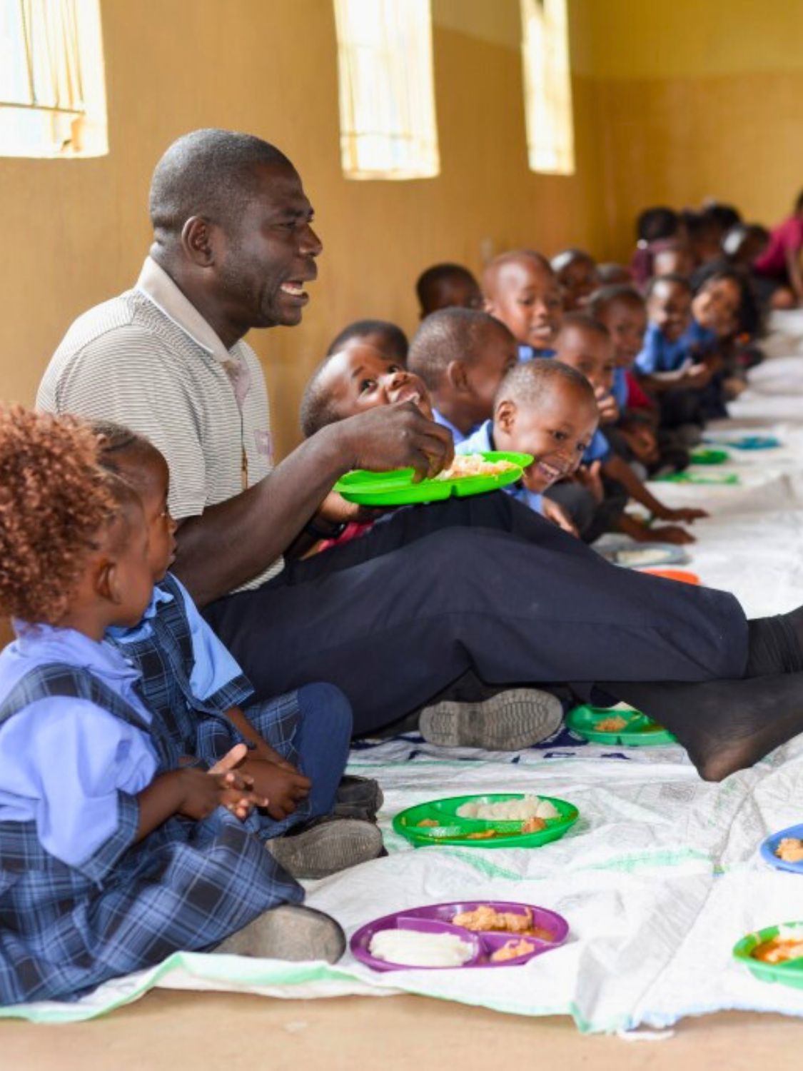 Pater Daniel, Schulleiter der Maria Regina Schule in Sambia, bringt Kinder beim gemeinsamen Essen zum Lachen.