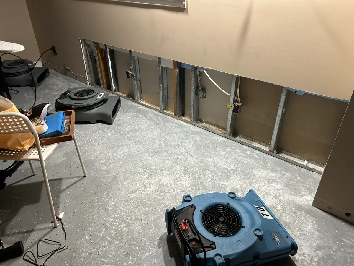Room with drywall removed on lower wall and air movers drying the floor after water damage.