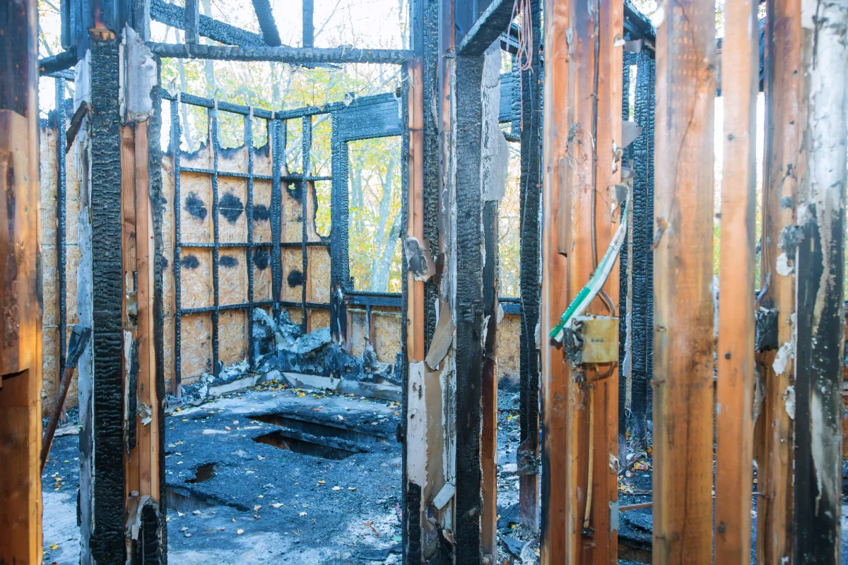 Interior of a burnt structure with charred wooden beams and walls, and a damaged floor.